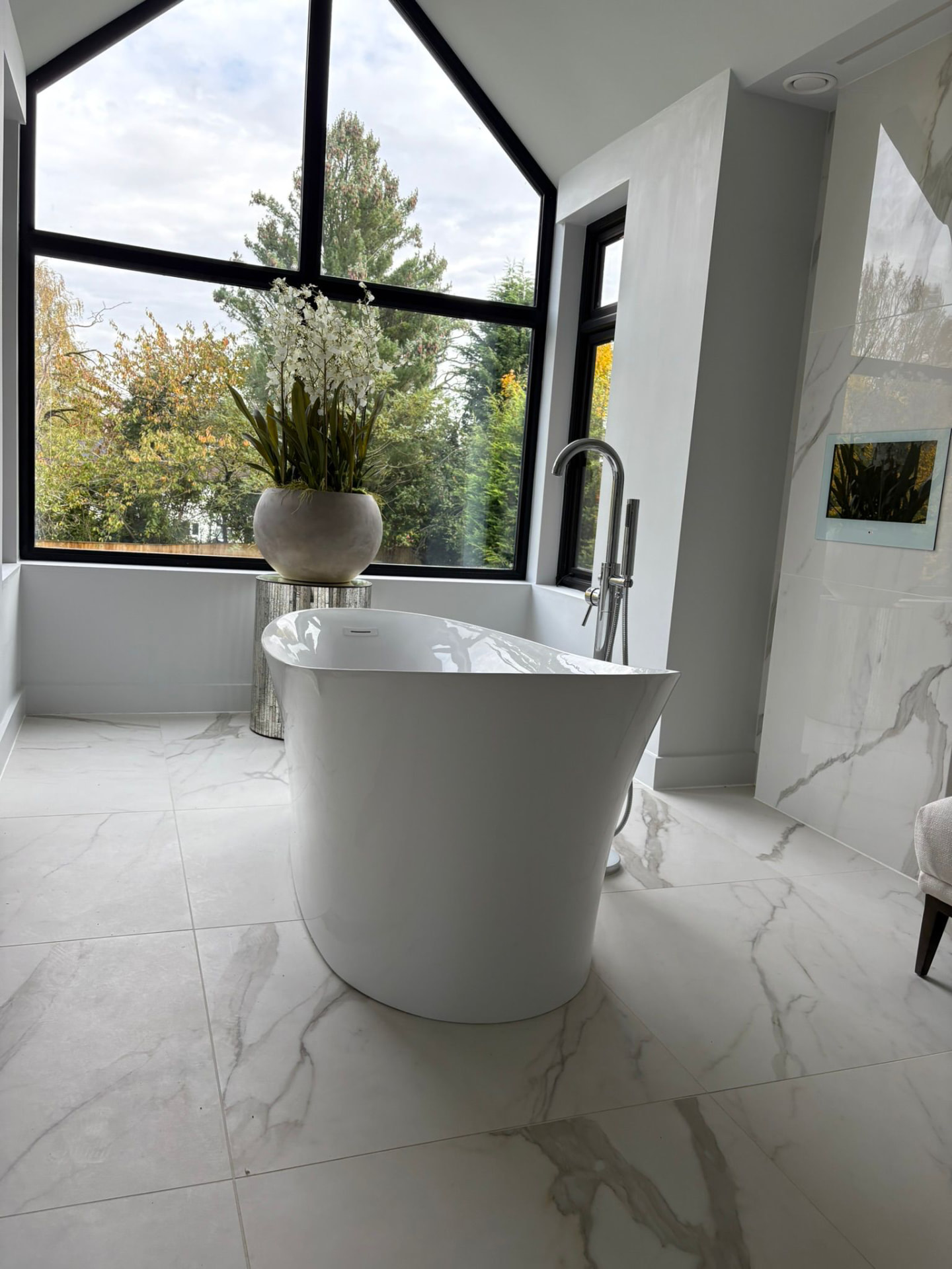 Modern freestanding bath in a bright bathroom with marble tiles and large windows